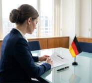 Cadre français lisant un contrat de travail allemand sur un bureau avec un drapeau de l'Allemagne.