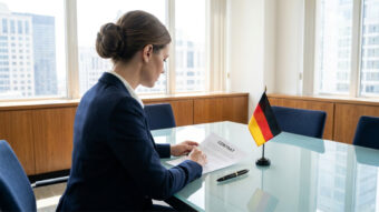 Cadre français lisant un contrat de travail allemand sur un bureau avec un drapeau de l'Allemagne.